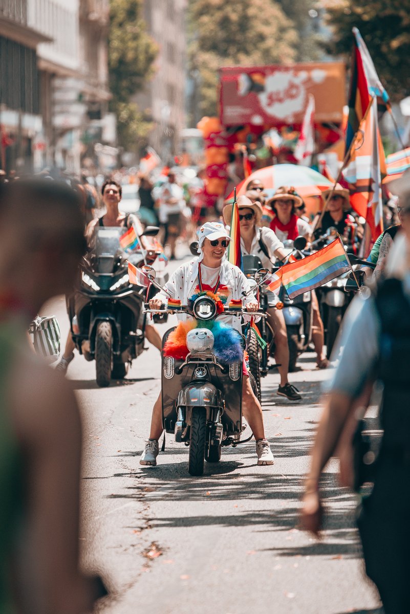 Teilnehmende auf geschmückten Motorrollern und Motorrädern fahren mit Regenbogenflaggen durch die Münchner Pride-Parade.