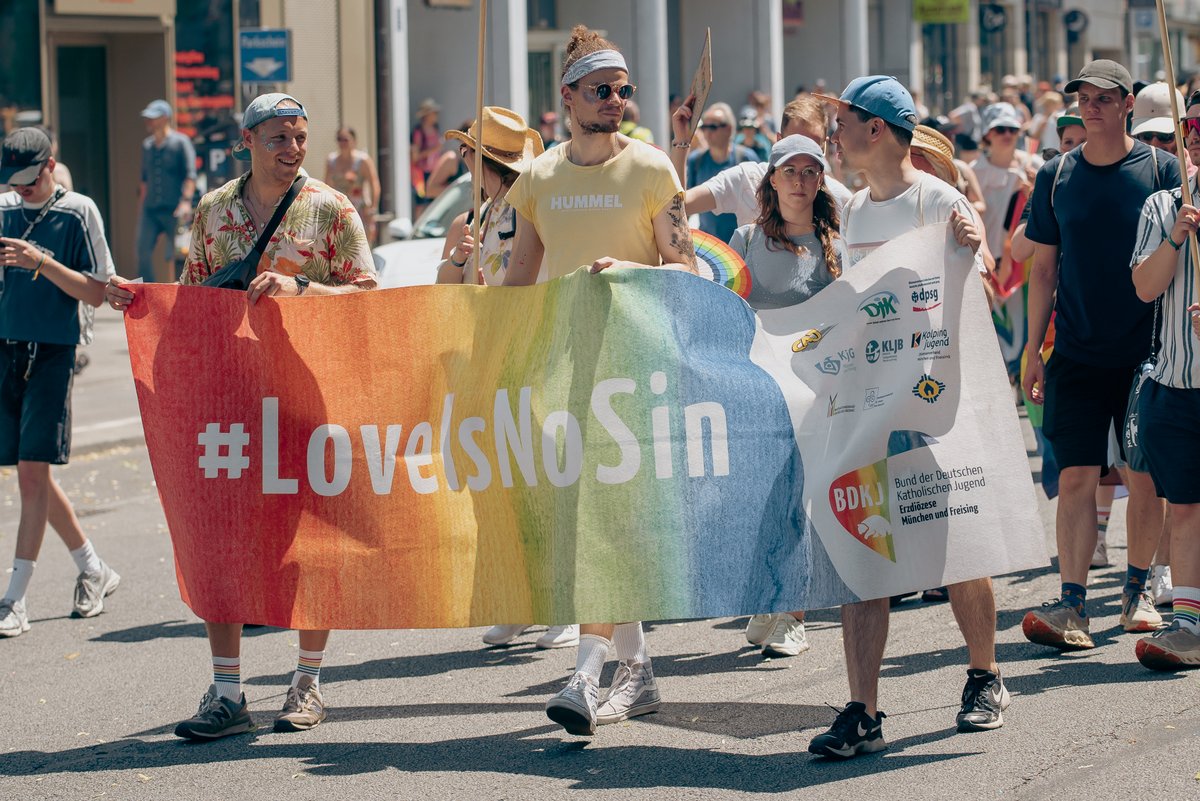 Gruppe junger Menschen tr?t ein gro?s Banner mit der Aufschrift ?#LoveIsNoSin? durch die M?chner Pride-Parade.