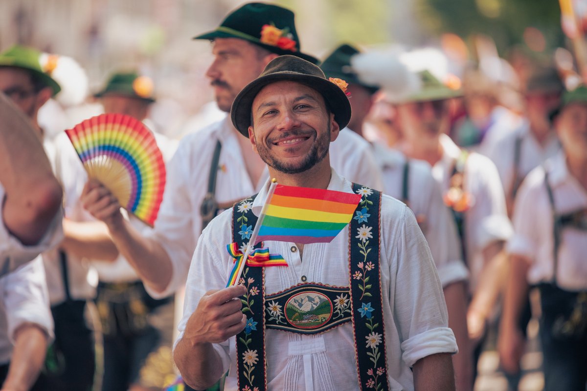 L?helnder Teilnehmer mit Regenbogenf?her und Pride-Aufn?er l?ft in der Parade mit.