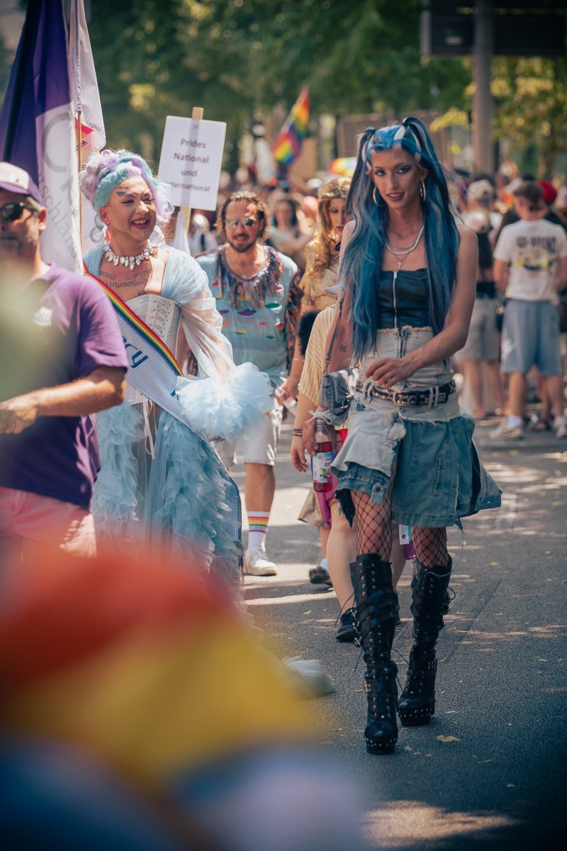 Person in Leder-Outfit geht an der Paradestrecke entlang, umgeben von Zuschauenden und Pride-Flaggen.