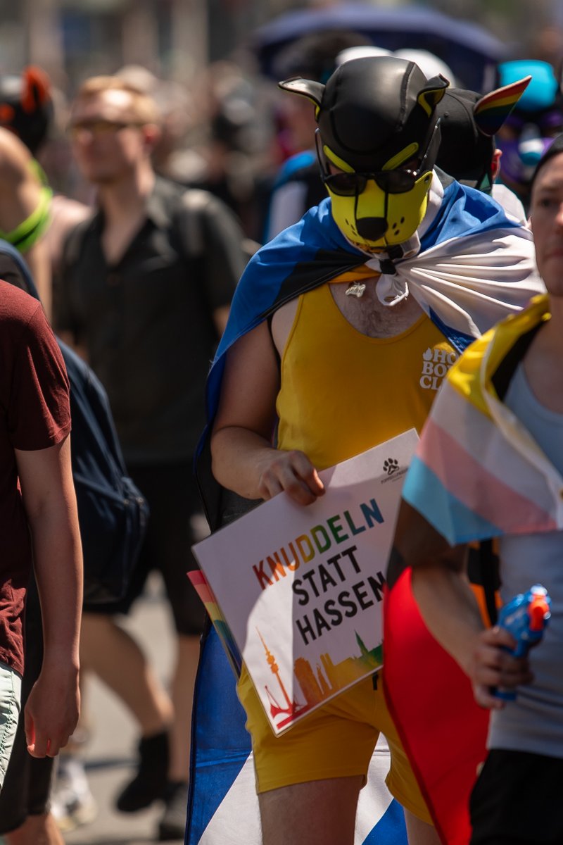 Teilnehmender in gelb-blauem Kost? und Kopfbedeckung l?ft zwischen weiteren Pride-G?ten.