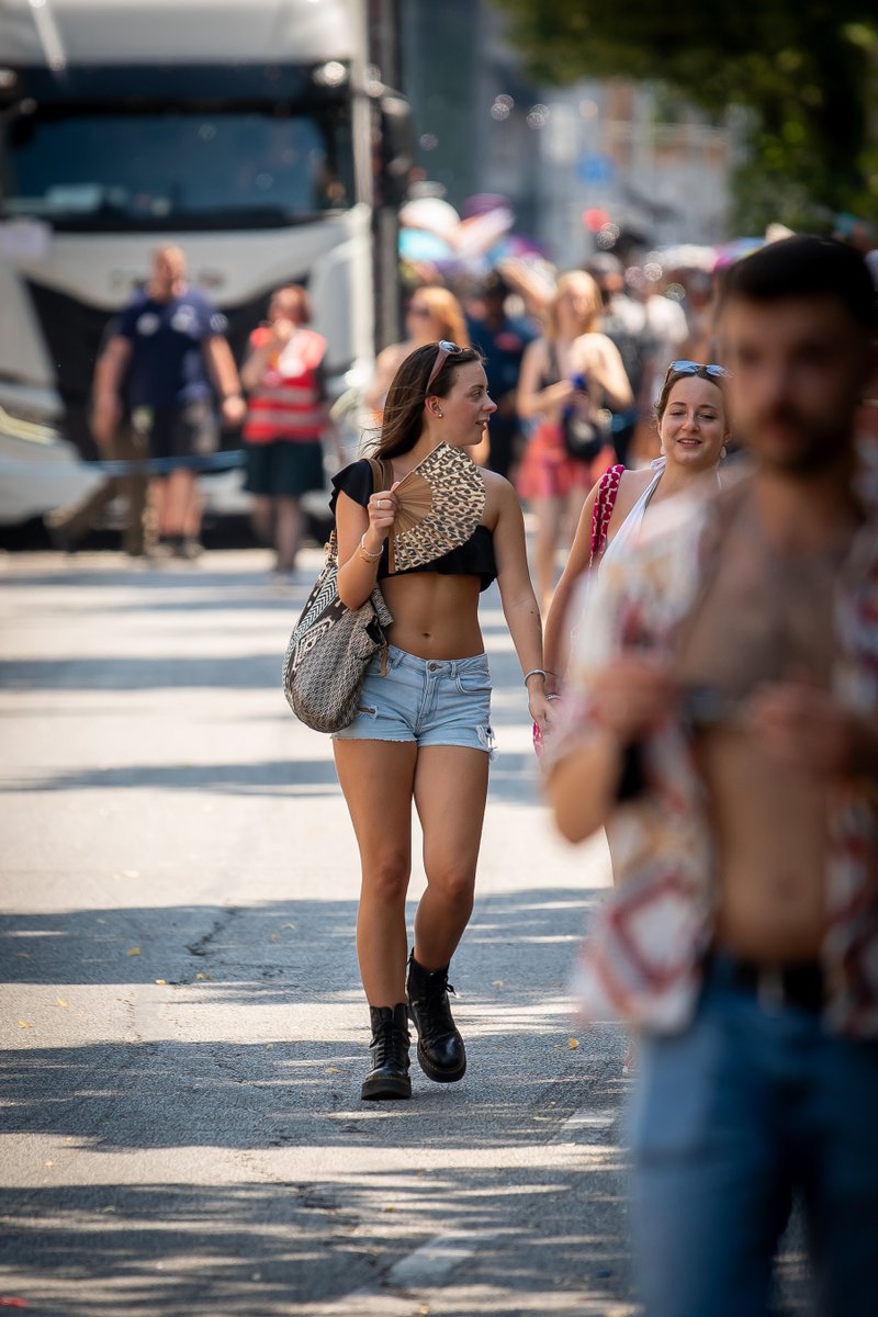 Junge Frau l?ft durch die Stra?, w?rend die Pride-Parade im Hintergrund vorbeizieht.