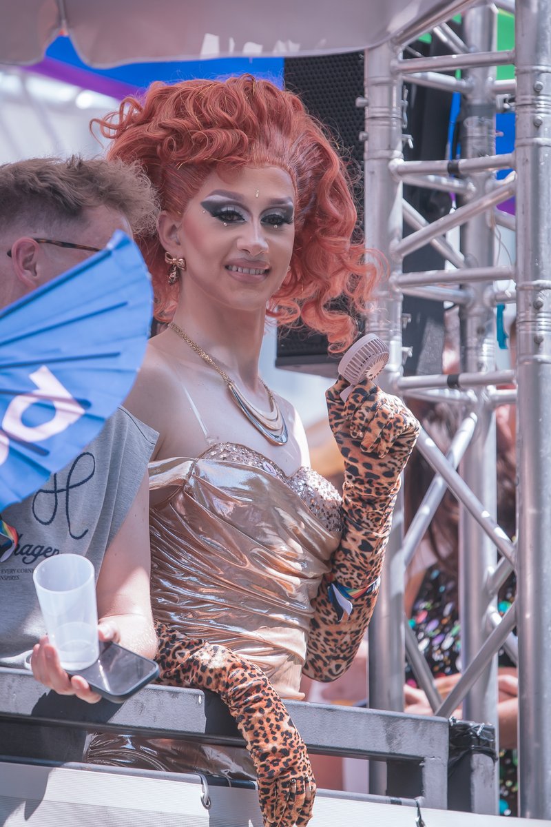 Drag Artist mit kupferfarbenem Kleid steht auf einer B?ne oder einem Wagen und blickt in die Kamera.
