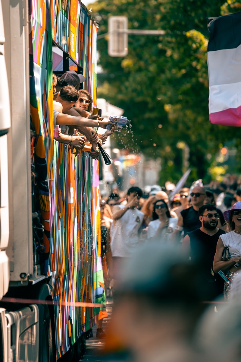 Blick entlang eines Paradewagens mit Regenbogenb?dern und winkenden Teilnehmenden.