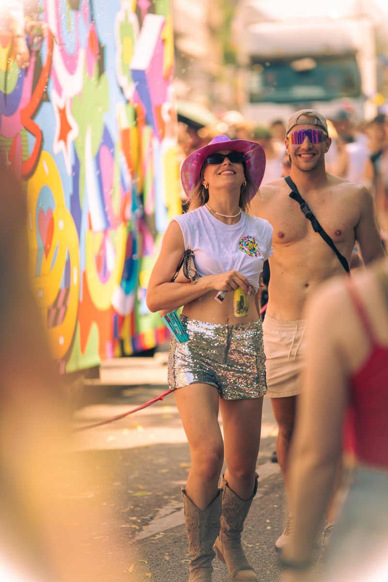 Lachende Teilnehmerin in silbernem Outfit und Sonnenbrille steht zwischen Pride-G?ten.