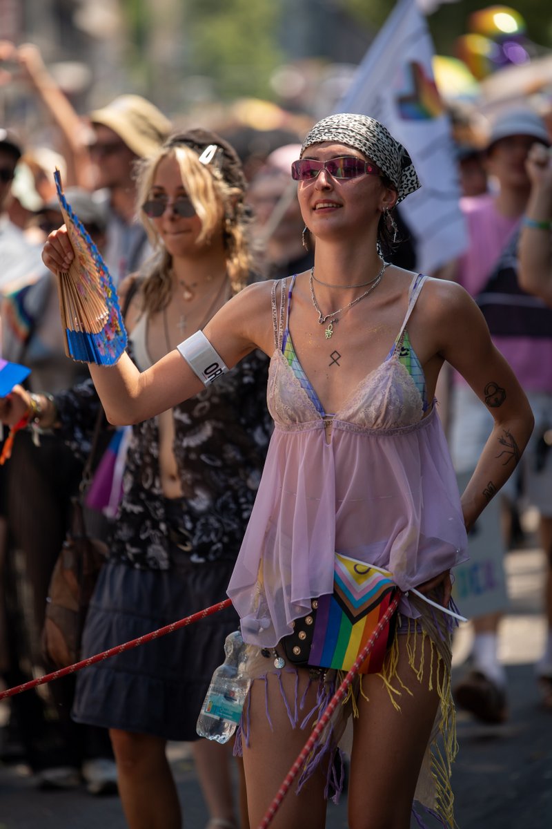 Junge Frau mit Pride-F?nchen blickt begeistert zur Parade und hebt den Arm.