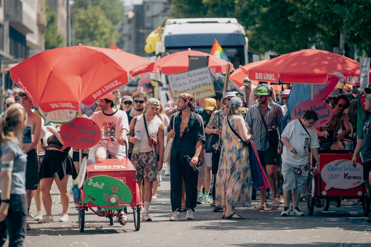 Gruppe mit roten Sonnenschirmen und Kinderwagen wartet am Rand der Paradestrecke.
