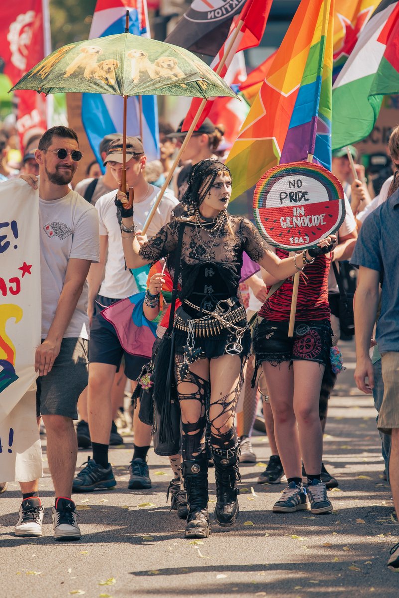Gruppe in schwarzen Outfits posiert mit Regenbogenflaggen und runden Pride-Schildern.