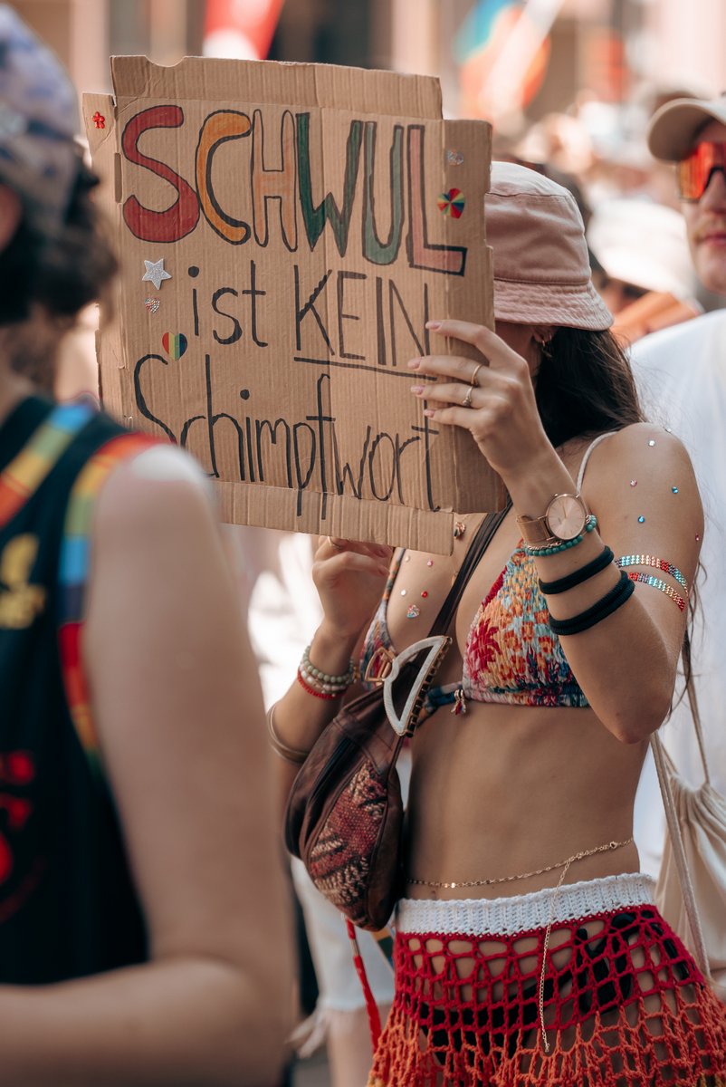 Person h?t ein Schild mit humorvoller Botschaft ?er queere Sichtbarkeit hoch.