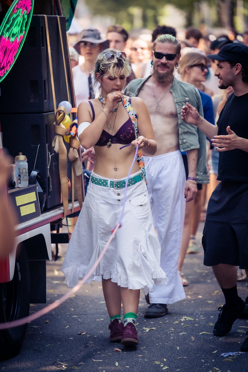 Teilnehmerin in wei?m Rock und Pride-Accessoires l?ft neben einem Wagen durch die Parade.