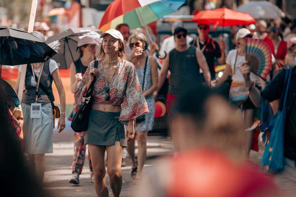 Drei Teilnehmende laufen gemeinsam durch die Pride-Parade, umgeben von Zuschauerinnen und Zuschauern.