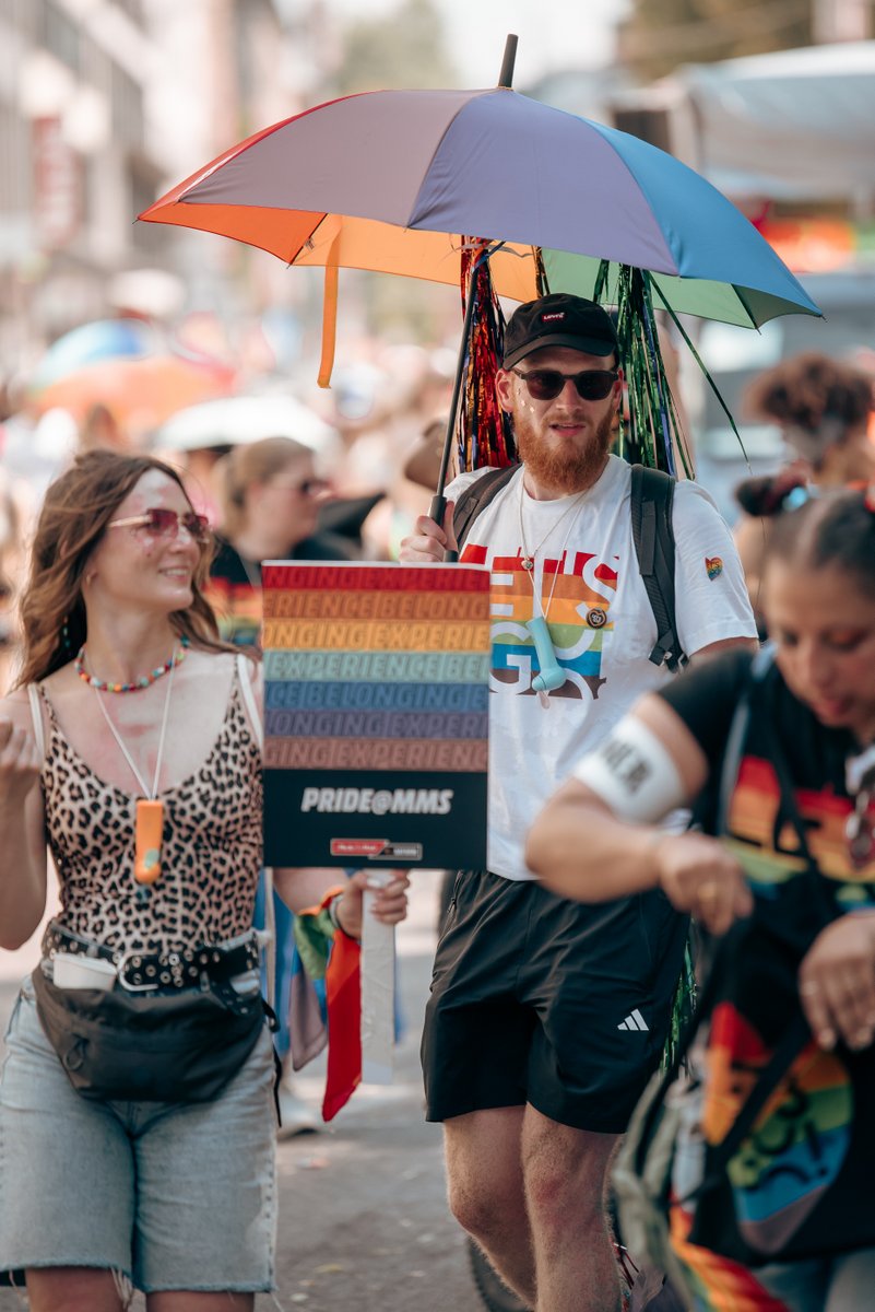 Teilnehmer mit Regenbogenschirm und Schild steht inmitten der Parade.