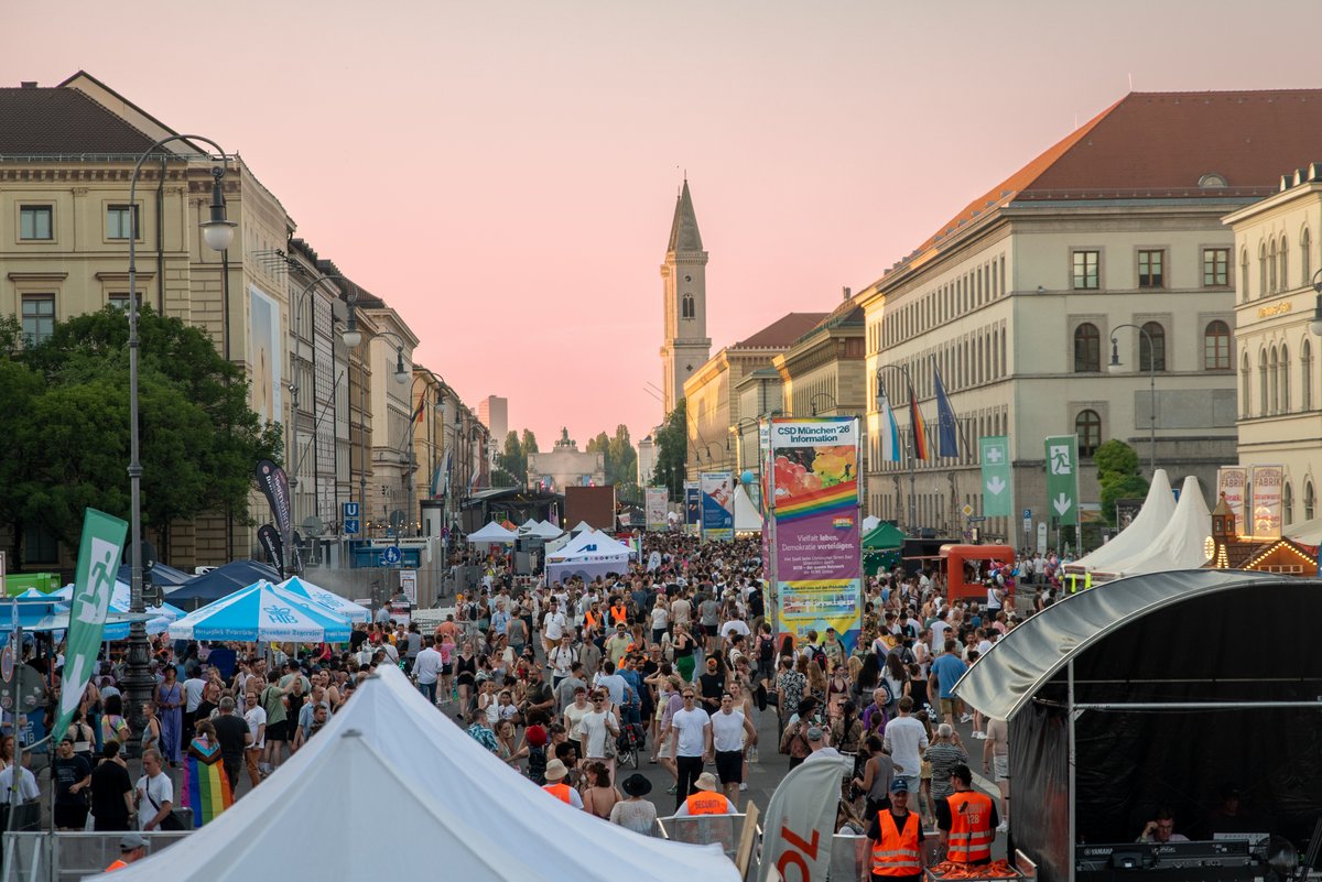 Abendlicher Blick ?er ein volles Stra?nfest mit St?den, Fahnen und beleuchteter Kirche im Hintergrund.