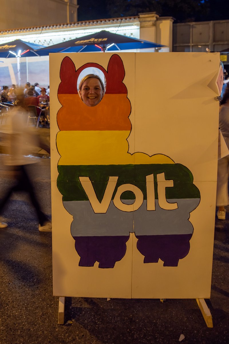 Volt-Wahlplakat mit gezeichneter Figur steht am Abend am Rand des CSD-Festgel?des.