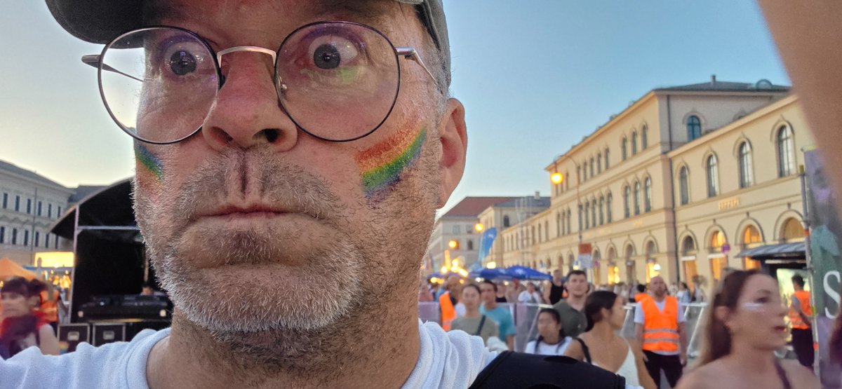 Nahes Selfie eines Besuchers mit Regenbogenbemalung im Gesicht inmitten der Abendveranstaltung.