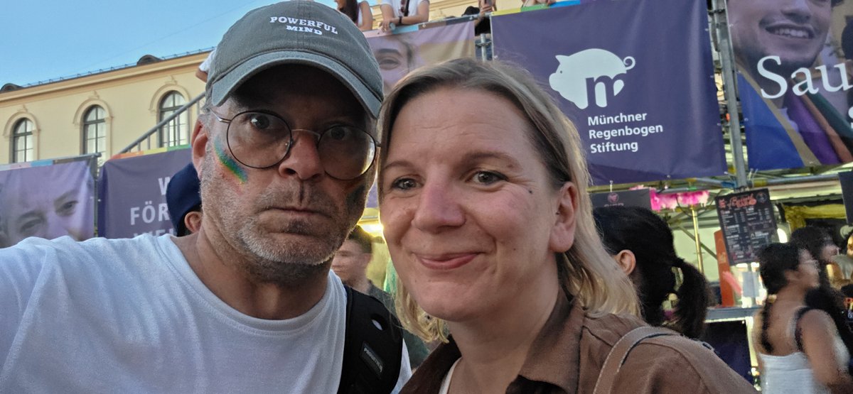 Selfie eines Paares vor der B?ne und Menschenmenge beim abendlichen Pride-Fest.